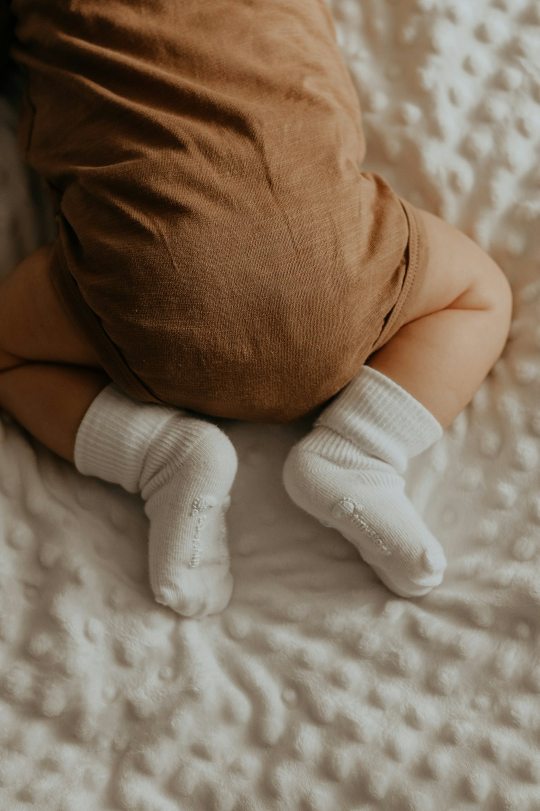 baby in white socks lying on bed