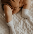 baby in white socks lying on white bed