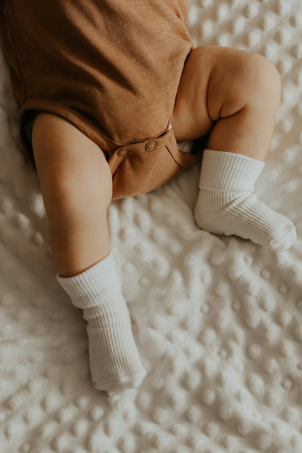 baby in white socks lying on white bed