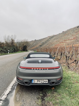 A sleek Porsche 911 driving past the green hills of the Nürburgring on a sunny day.
