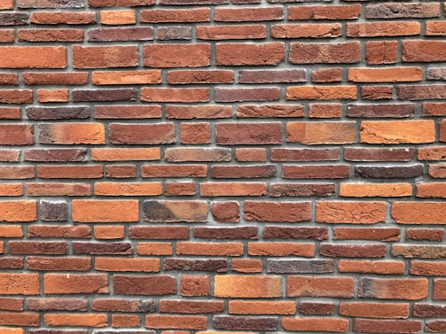 A pattern of red and orange bricks arranged in a horizontal layout, featuring variations in texture and shade. The mortar lines between the bricks are visible and uniform, providing a consistent and orderly appearance.