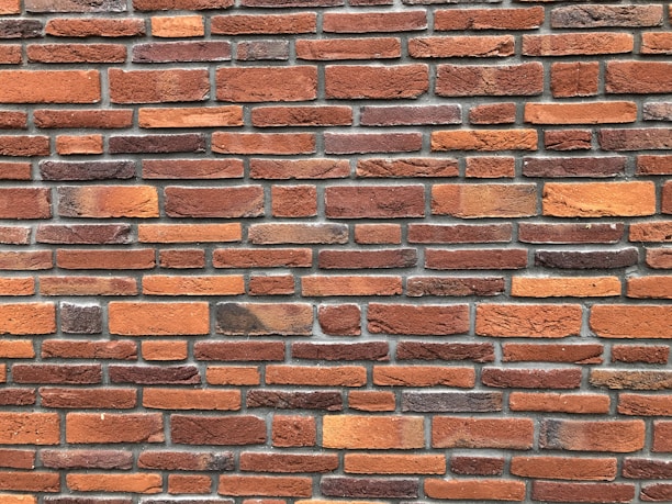 A pattern of red and orange bricks arranged in a horizontal layout, featuring variations in texture and shade. The mortar lines between the bricks are visible and uniform, providing a consistent and orderly appearance.