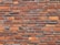 A pattern of red and orange bricks arranged in a horizontal layout, featuring variations in texture and shade. The mortar lines between the bricks are visible and uniform, providing a consistent and orderly appearance.