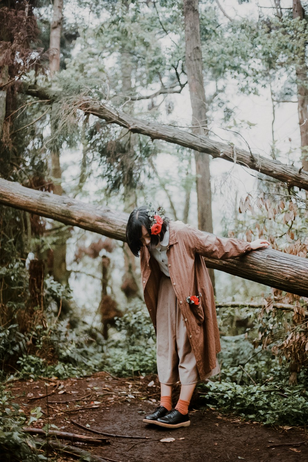 woman in brown coat standing on tree branch during daytime