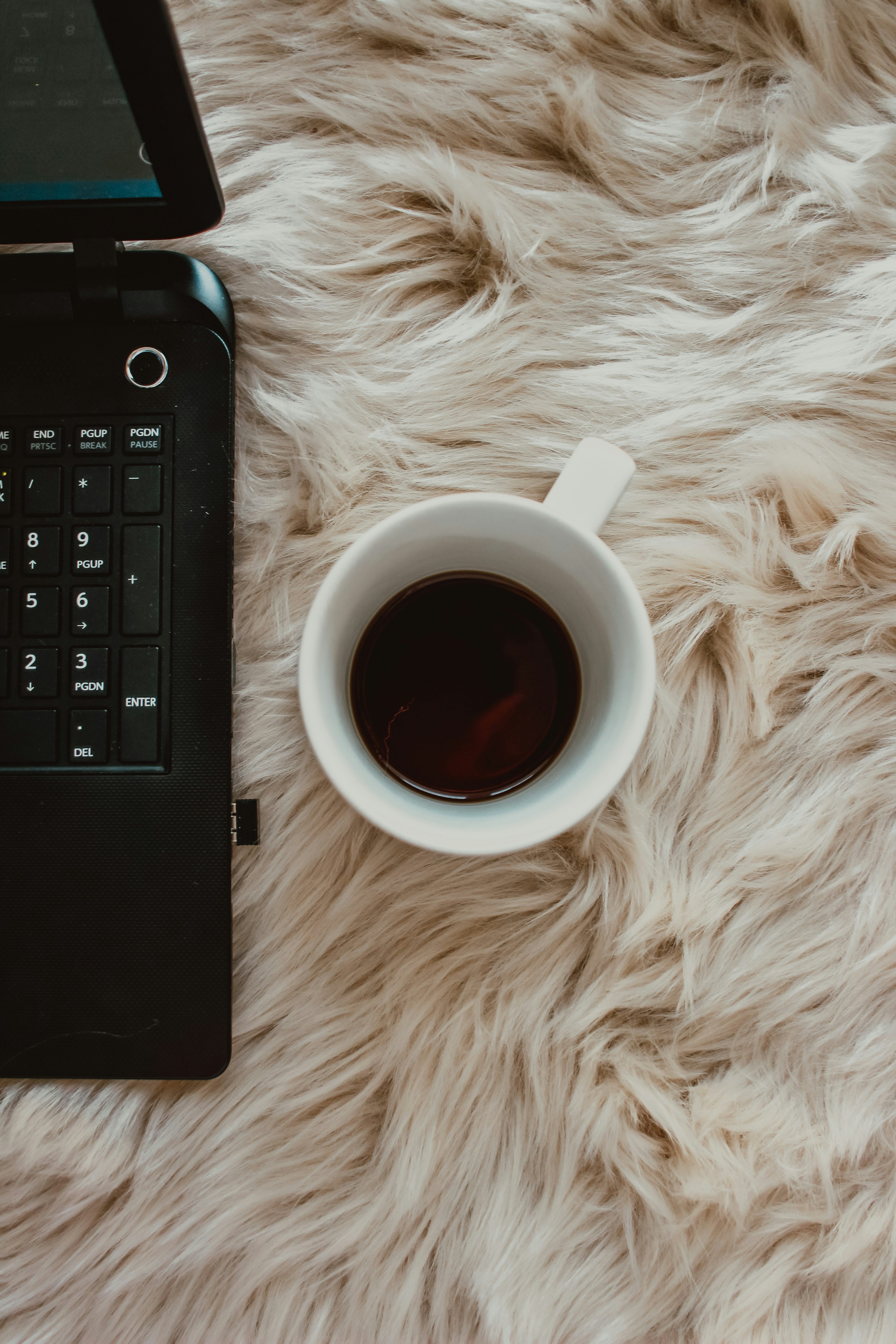 Laptop and coffee mug on a fluffy beige blanket.