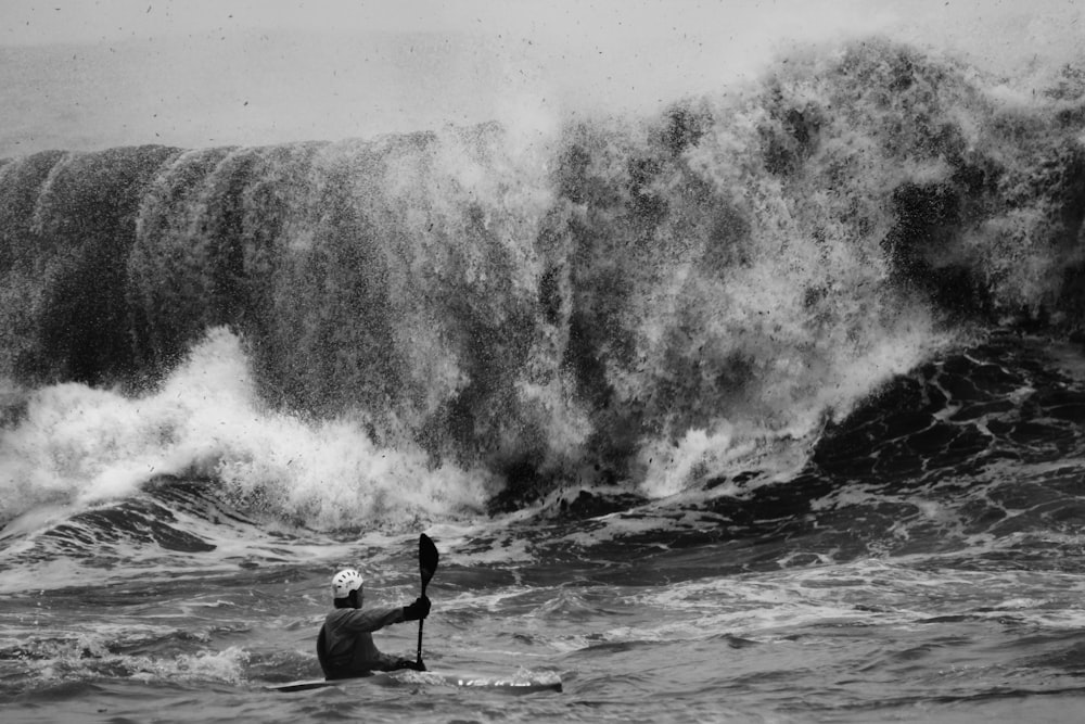 grayscale photo of person standing on sea waves