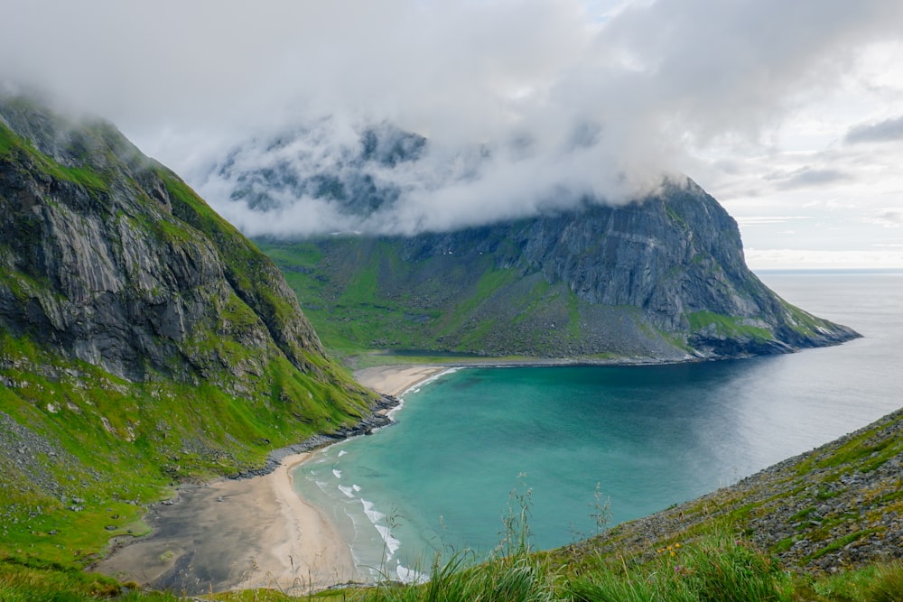 green mountain beside body of water under cloudy sky during daytime