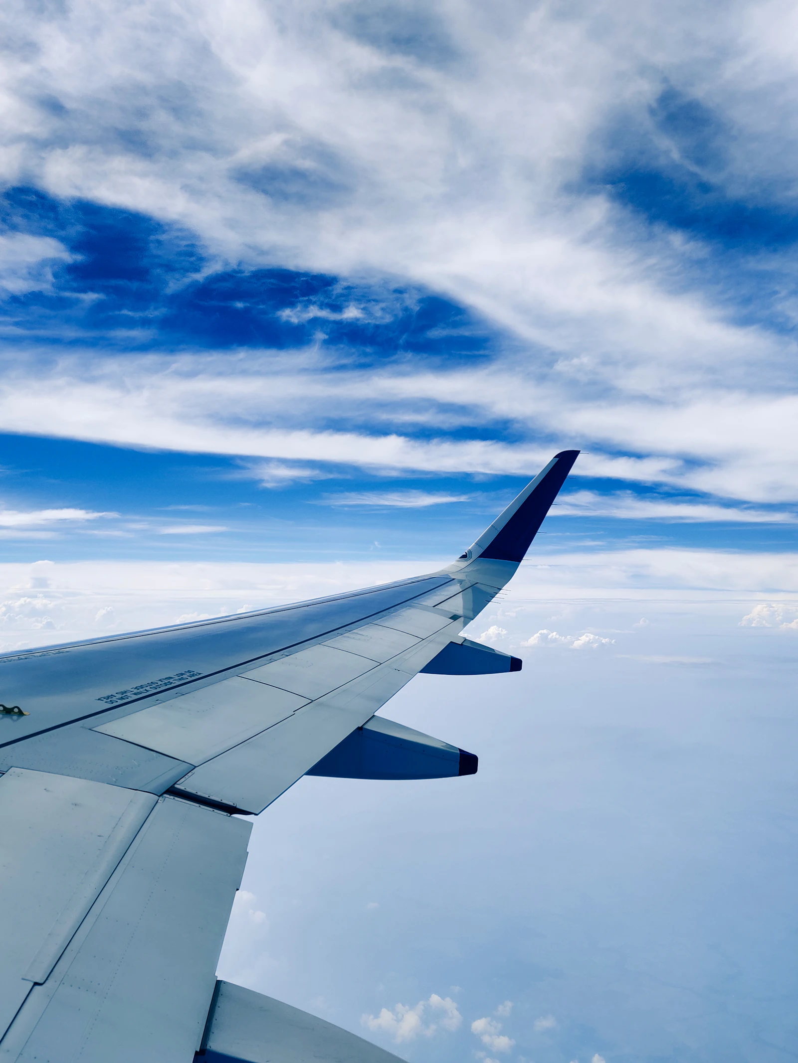 View of an airplane wing above a bank of white clouds under a clear blue sky in calm daylight
