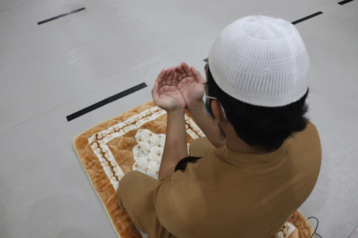 A certified Muslim fitness advisor gently guiding an elder in light stretching exercises inside a mosque hall.