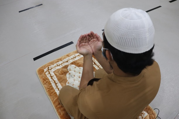A warm, inviting photo of Maalim Rashid praying with hands raised in a peaceful setting.