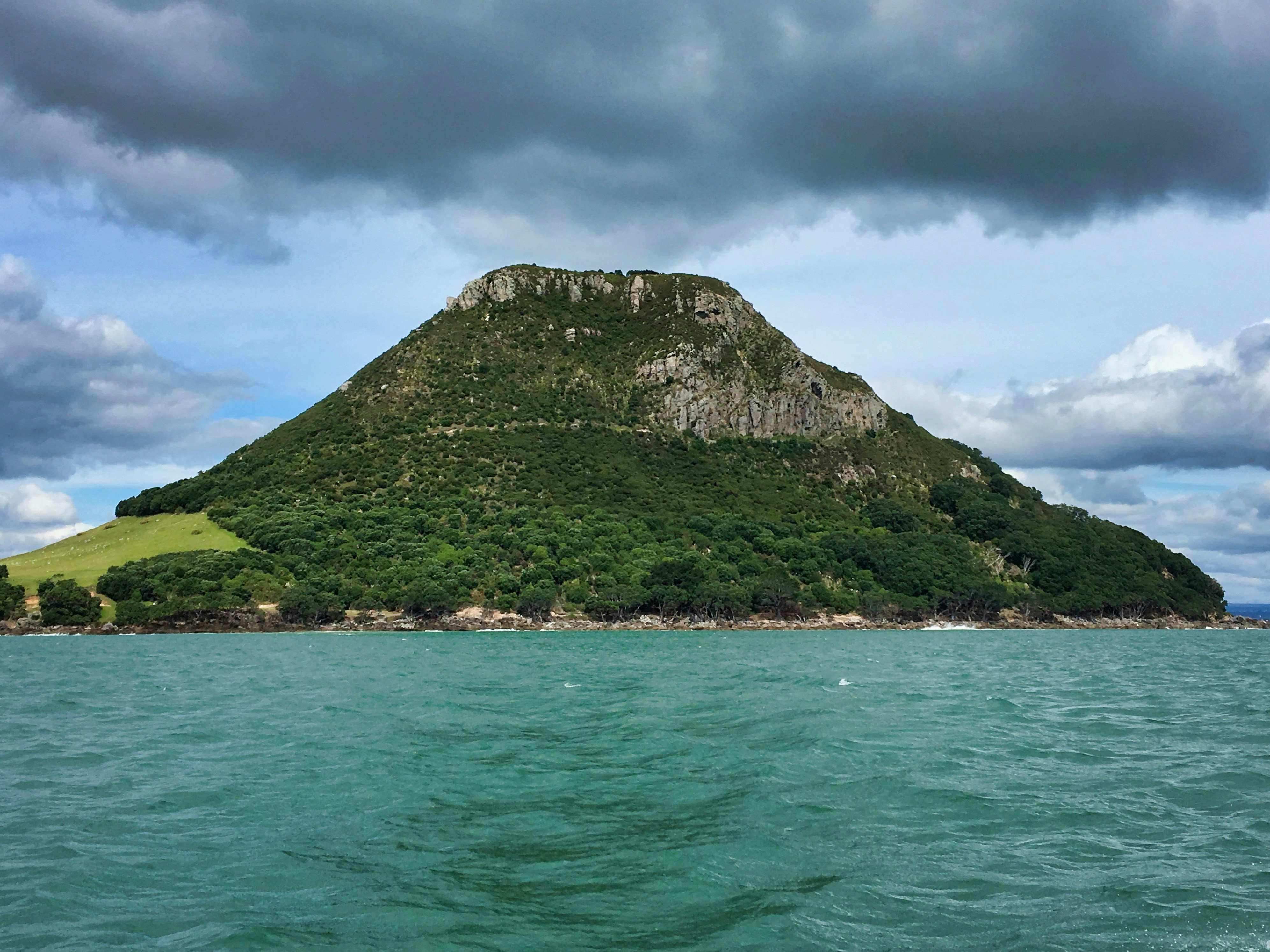 green mountain beside body of water under cloudy sky during daytime, Amazing rock mountain in Bay Of Plenty, New Zealand.