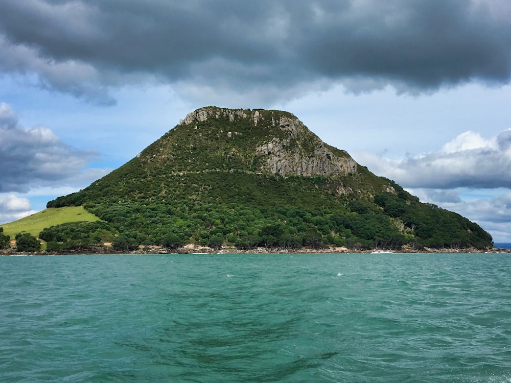 montagna verde accanto allo specchio d'acqua sotto il cielo nuvoloso durante il giorno