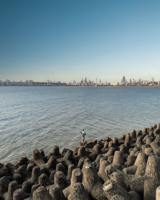 person in green shirt standing on rock formation near body of water during daytime