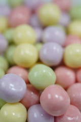 A pile of glossy, spherical candies showing a mix of pastel colors including yellow, pink, green, and lavender. The candies are closely packed together, creating a vibrant and colorful texture.