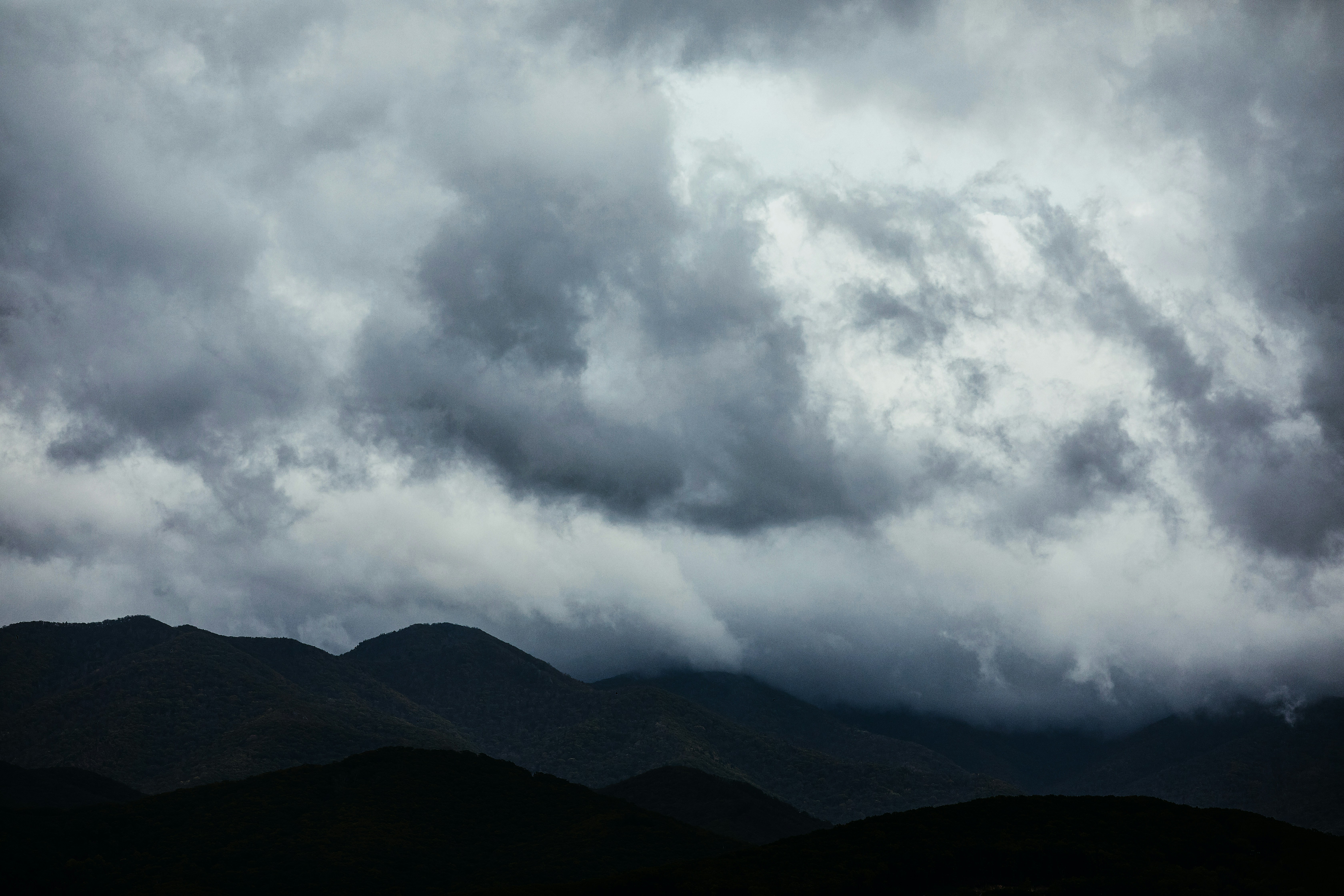 Travel content creator filming at scenic location, overcast moody sky, dark mountain silhouettes, atmospheric low light environment