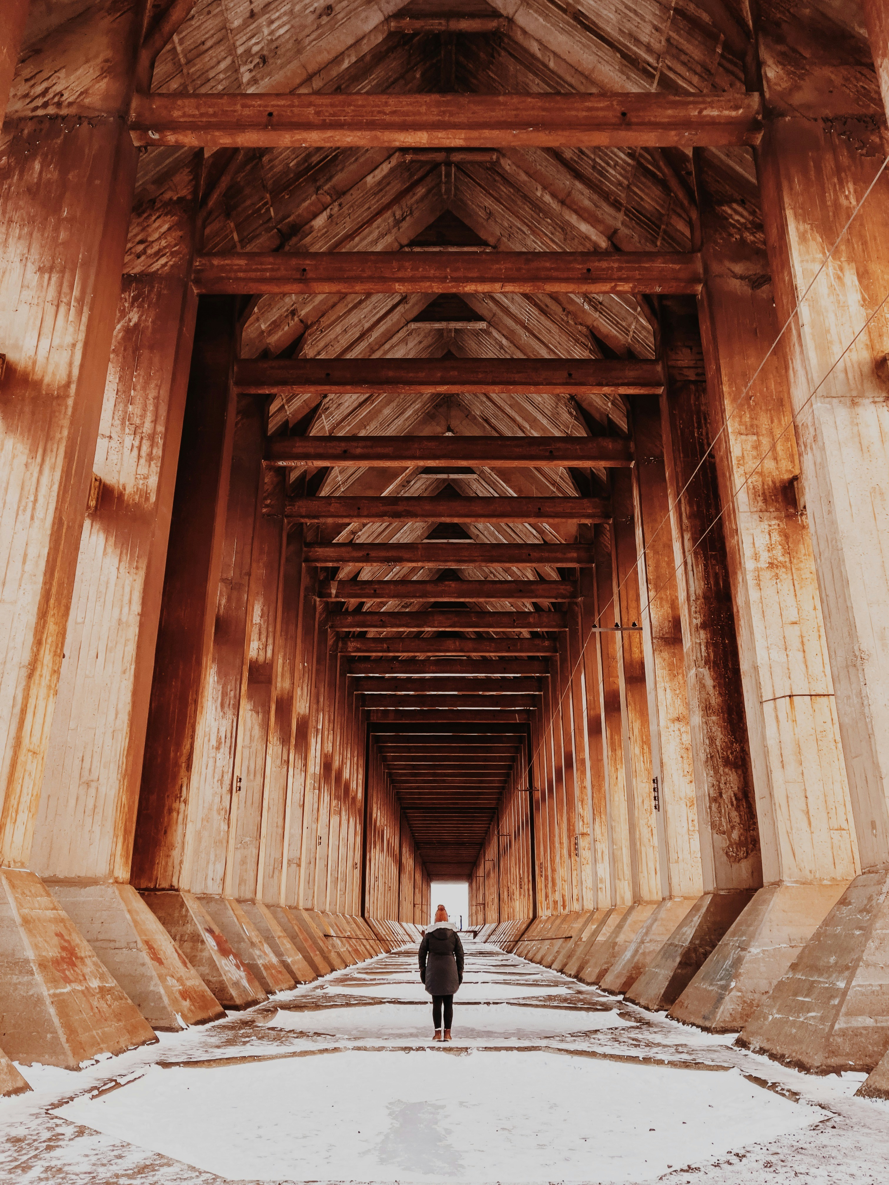person in black jacket walking on brown wooden bridge