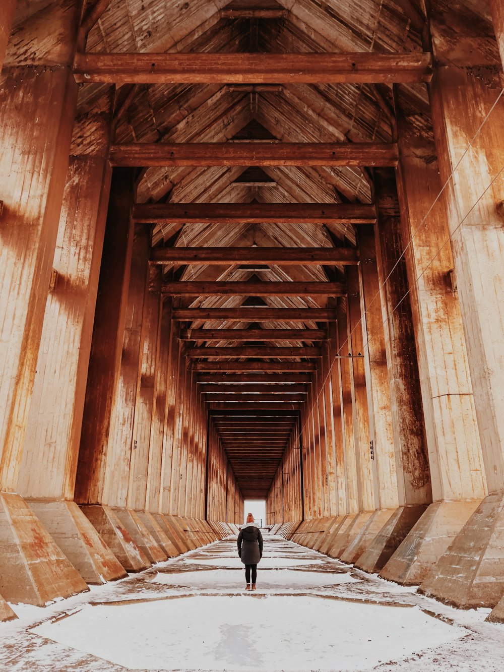 person in black jacket walking on brown wooden bridge