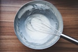 Hands gently whisking a creamy sauce in a sleek stainless steel bowl.