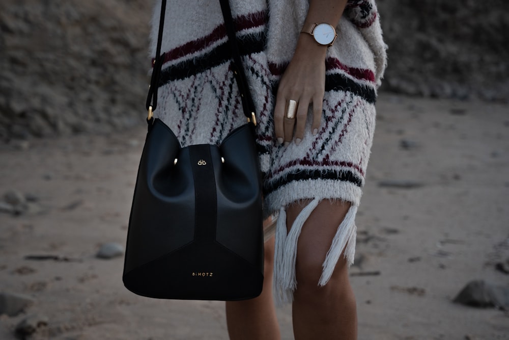woman in white knit sweater holding black leather handbag