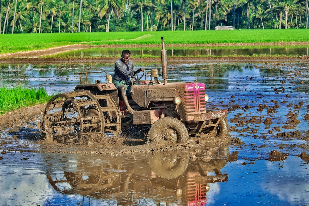 man in black jacket riding red tractor on river during daytime