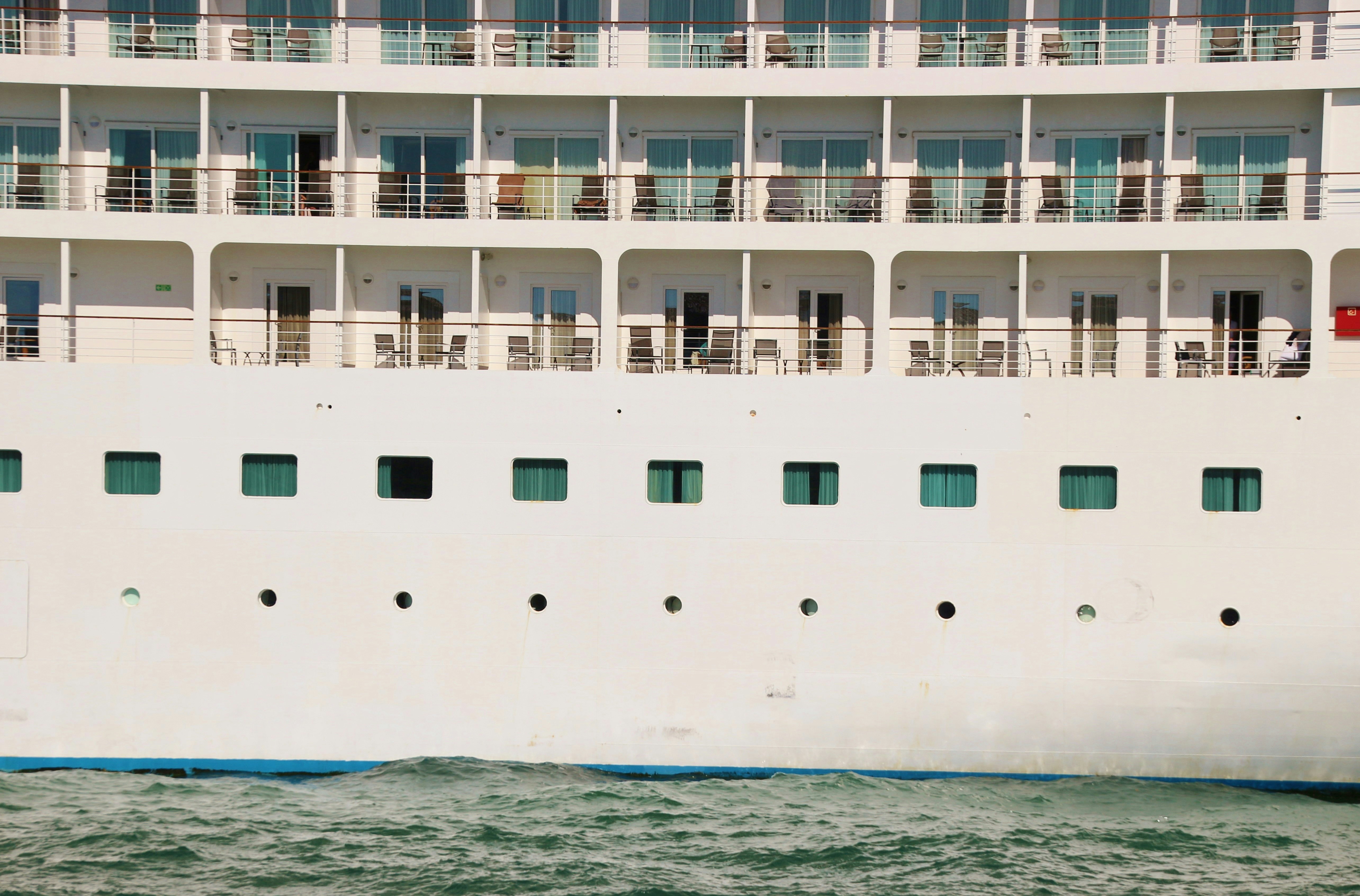 white and blue cruise ship on blue sea during daytime, Close-up view of a huge cruise ship in the harbor of Venice, district Santa Croce. Balconies and chairs, no passengers are on board. Italy, Europe.