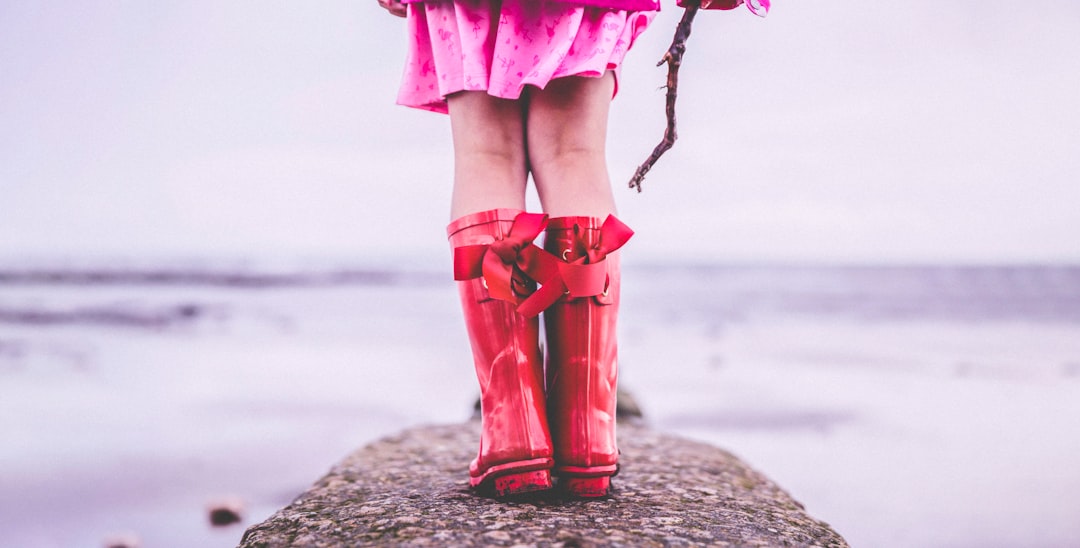 woman in pink dress and red boots standing on beach shore during daytime