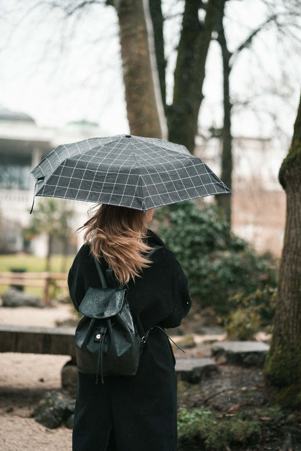 Frau im schwarzen Mantel mit Regenschirm