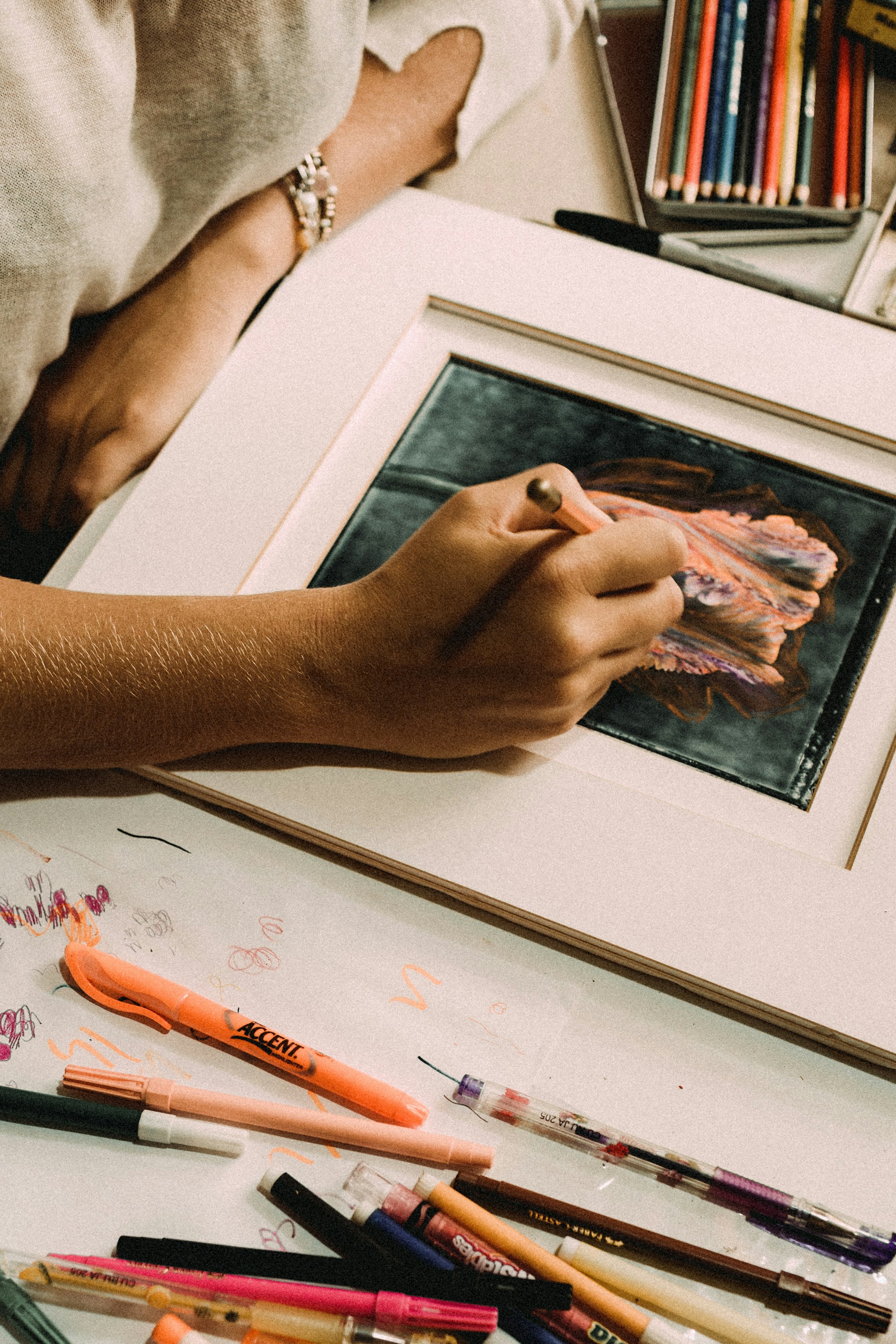 An artist's hand mid-sketch, surrounded by an array of sharpened colored pencils in a sunlit studio.