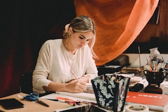 A close-up of Pilar Lozano Riveros writing at her desk with a warm red-toned background.