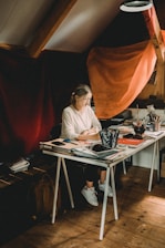 Portrait of Kota McKinnon sitting at a rustic wooden desk surrounded by notebooks and a laptop.