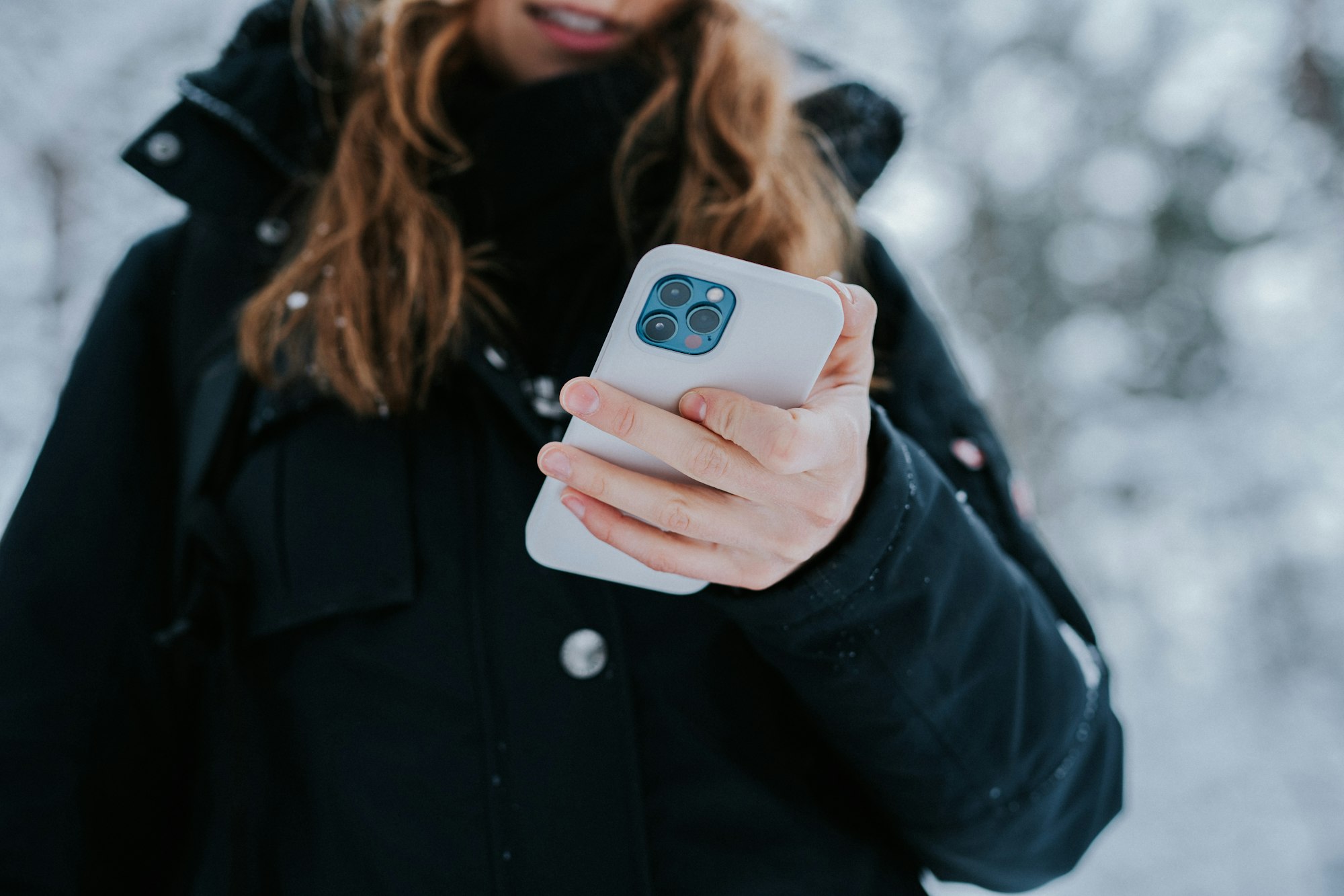 A woman holding an iphone 12 taking pictures and discovering her timeline on her smartphone. Outside in winter checking her phone. If you like link our website https://www.dieberater.de, we find your content via image backward search and even share your content if it's great. 