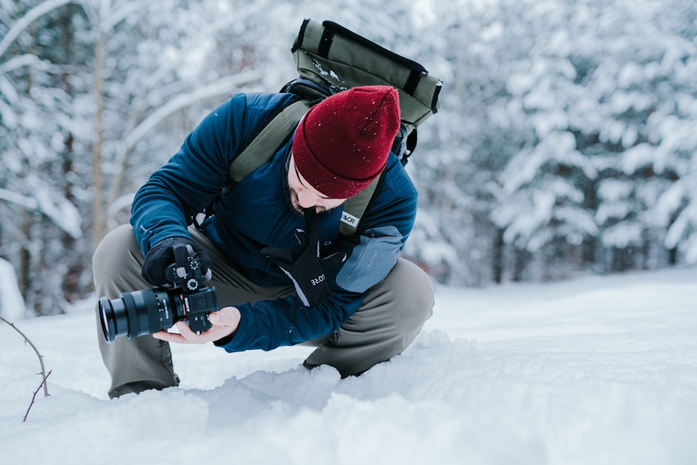 man in black jacket and red helmet holding black dslr camera on snow covered ground during