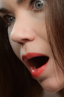 A dramatic close-up of a woman’s face illuminated by red light, eyes wide with shock and fear.