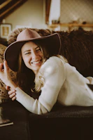 A relaxed model smiling while seated in a cozy room, dressed in a pastel Kaulika daster