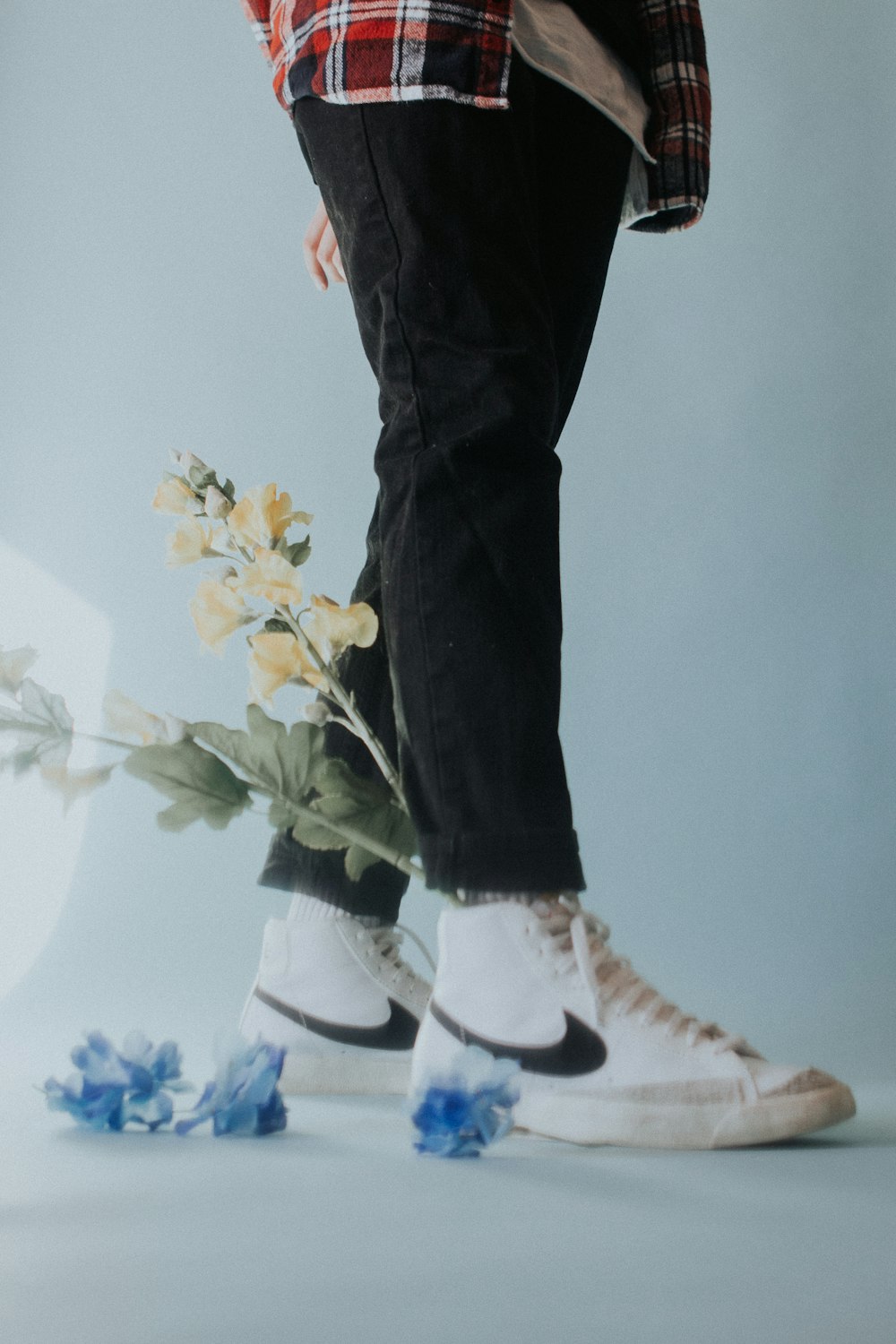 person in black pants and white sneakers standing beside yellow flowers
