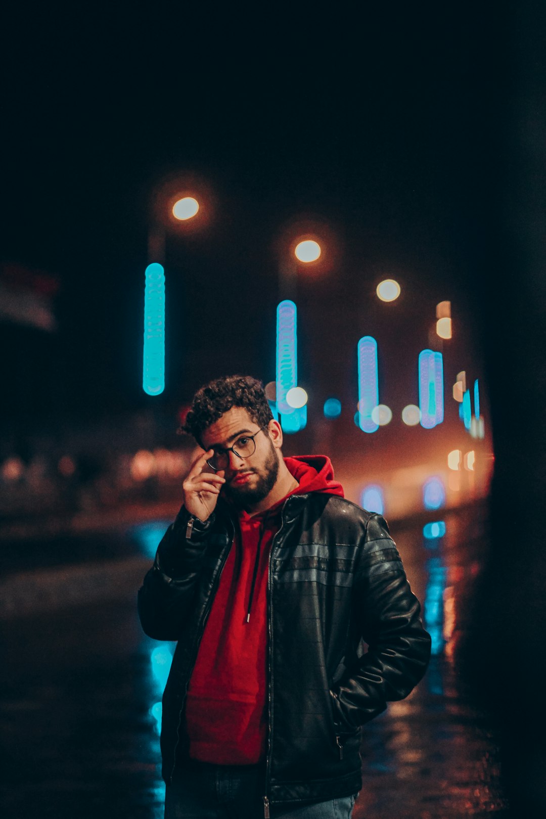 man in black leather jacket standing near street lights during night time