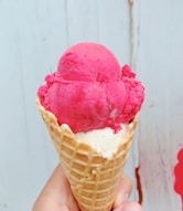 person holding ice cream cone with pink ice cream