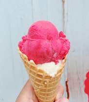 Close-up of colorful ice cream scoops in waffle cones against a white and pink background.