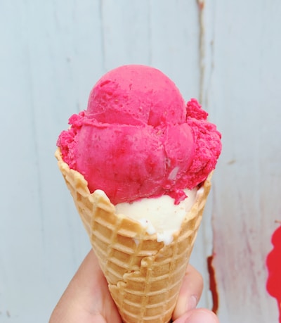 Close-up of colorful ice cream scoops in waffle cones against a white and pink background.