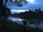 An elegant twilight shot of a calm lakeside with silhouetted trees and a single distant lantern glowing.