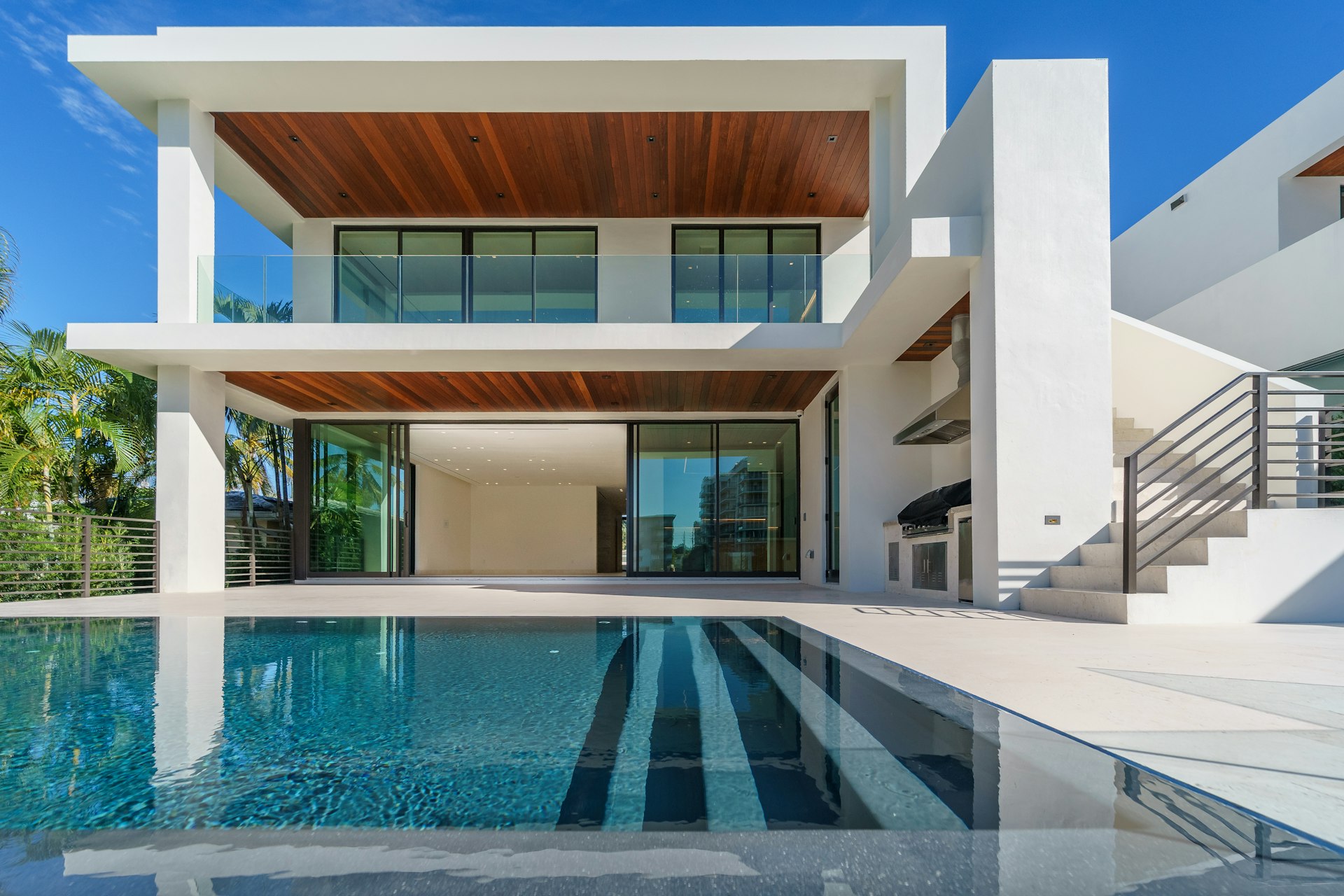 A modern house with a large pool in front of it. The house is white, and large sliding glass doors open onto the pool deck.