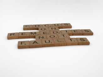 Scrabble tiles arranged to form the phrase 'FOCUS ON REMEDIES NOT FAULTS' on a white background.