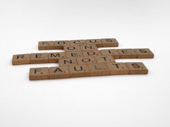 Scrabble tiles arranged to form the phrase 'FOCUS ON REMEDIES NOT FAULTS' on a white background.