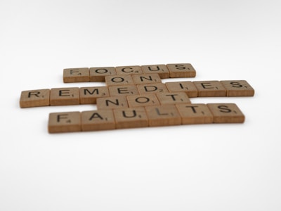 Scrabble tiles arranged to form the phrase 'FOCUS ON REMEDIES NOT FAULTS' on a white background.