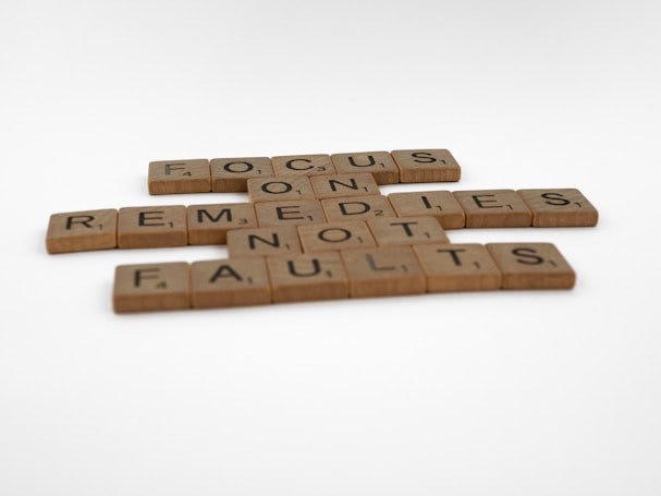 Scrabble tiles arranged to form the phrase 'FOCUS ON REMEDIES NOT FAULTS' on a white background.