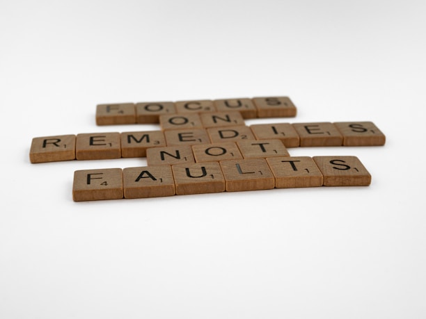 Wooden Scrabble tiles are arranged to form the motivational message: 'FOCUS ON REMEDIES NOT FAULTS'. The tiles are set against a plain, white background.