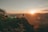 A person standing on a mountain peak, looking at a sunrise.