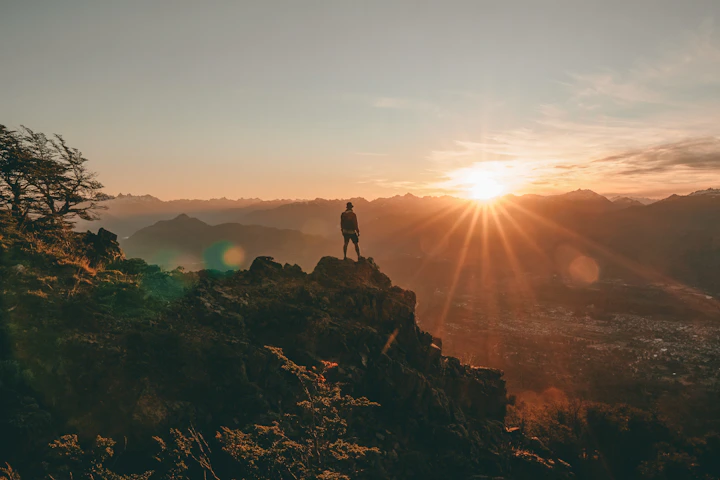A vibrant photo of a happy traveler standing on a mountain peak at sunrise, overlooking a breathtaking landscape.