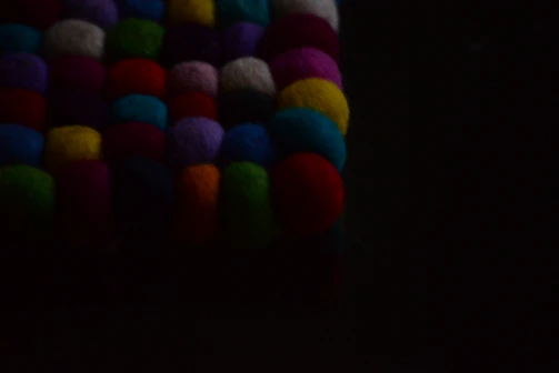 A vibrant close-up of colorful handmade yarn pom-poms scattered on a wooden table.