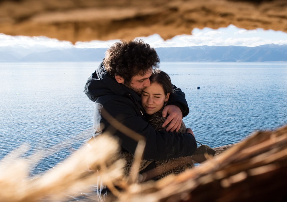 uomo e donna che si abbracciano vicino allo specchio d'acqua durante il giorno